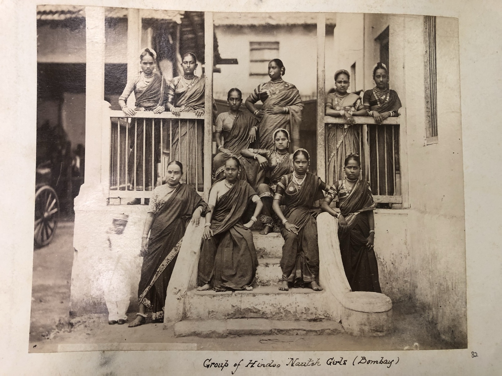 Album page: ten women photographed on the steps of a building in Bombay, captioned by hand "Group of Hindoo Nautch Girls (Bombay)"